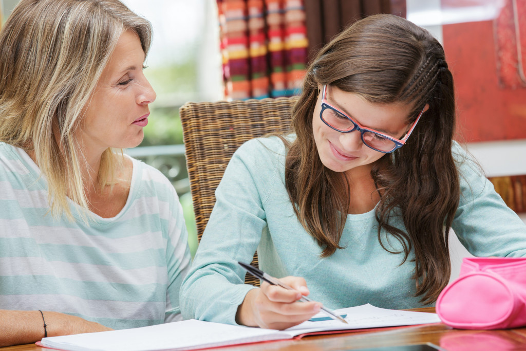 a young teen woman taking notes while sitting beside mother