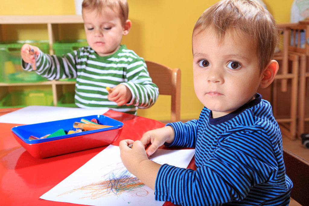 Toddlers using crayons on while pieces of paper.
