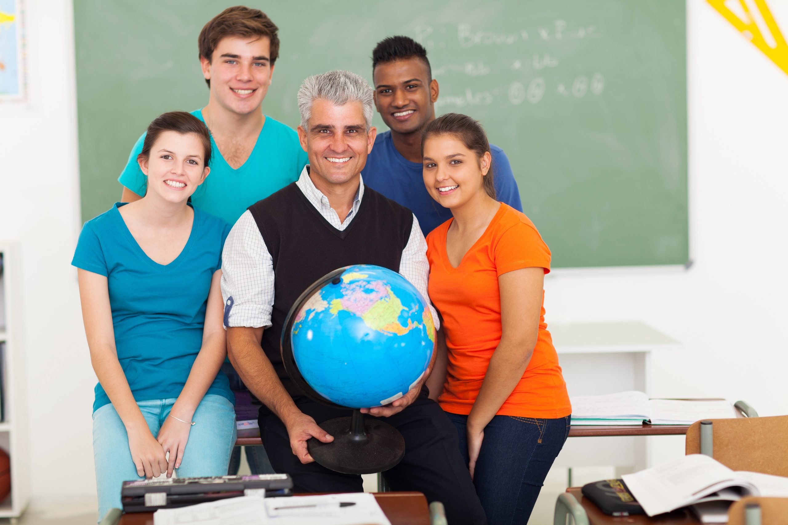 smiling male teacher holding a globe and with teen students